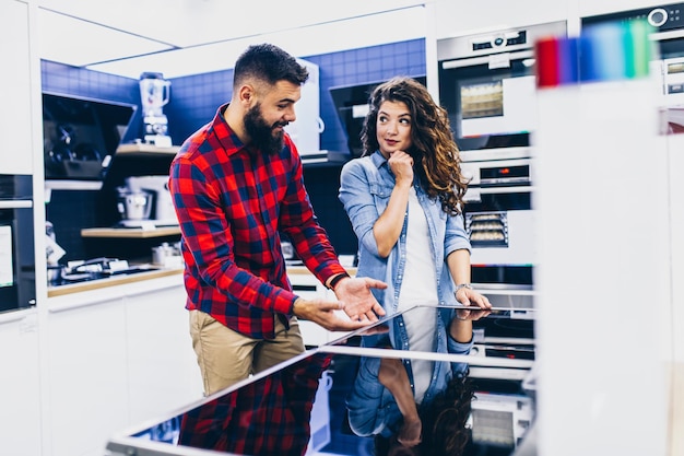 Heureux jeune couple achetant une table de cuisson électrique dans un magasin d'électroménagers.