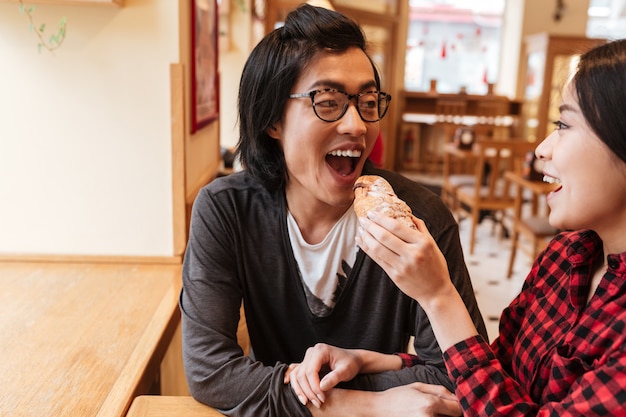 Heureux jeune couple aimant asiatique manger un croissant.