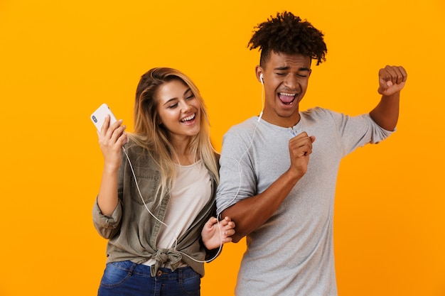 Heureux jeune couple d'amoureux dansant isolé sur mur jaune écoute de la musique par des écouteurs