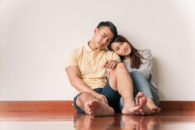 Heureux jeune couple asiatique assis sur le sol à la maison et levant les yeux avec espace de copie