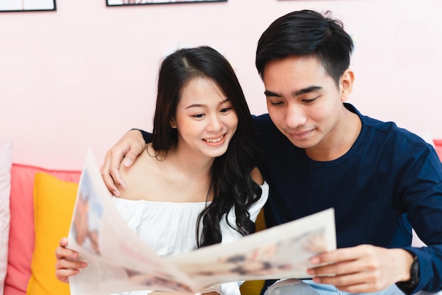 Heureux jeune couple asiatique à la maison. Se faire des câlins et passer du temps ensemble et lire un journal dans le salon