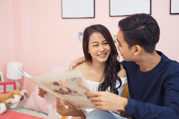 Heureux jeune couple asiatique à la maison. Se faire des câlins et passer du temps ensemble et lire un journal dans le salon