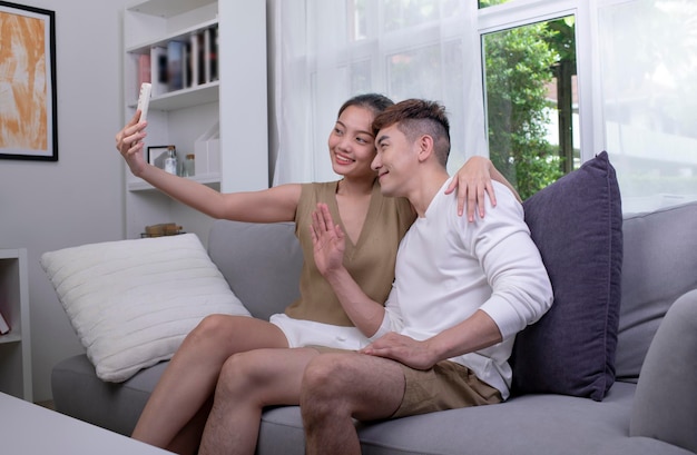 Heureux jeune couple asiatique prenant selfie sur le canapé dans le salon concept de style de vie couple homme et femme