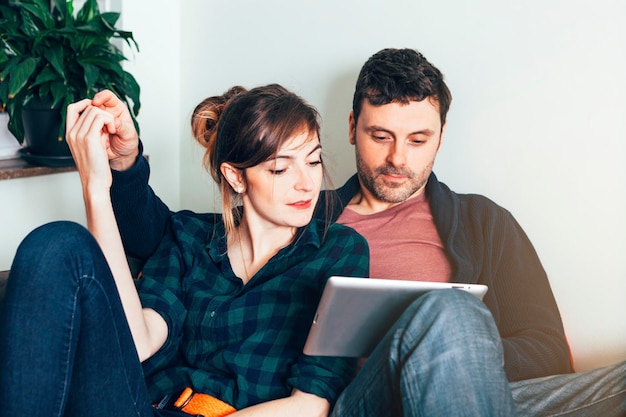 Heureux jeune couple assis sur le canapé et regardant sur une tablette