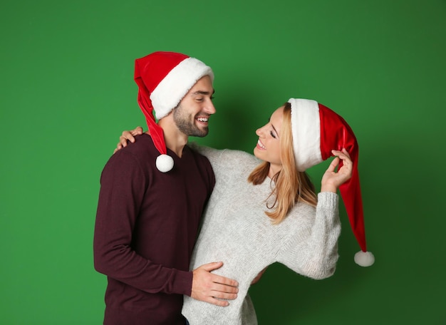 Heureux jeune couple en bonnets de Noel sur fond de couleur. Notion de Noël