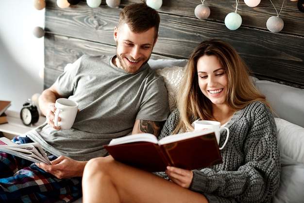 Heureux jeune couple avec café lecture au lit