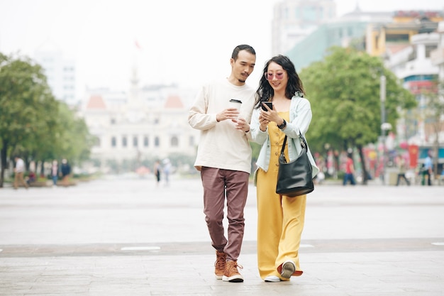 Heureux jeune couple chinois marchant sur la place de la ville et vérifiant la notification ou la carte sur smartphone