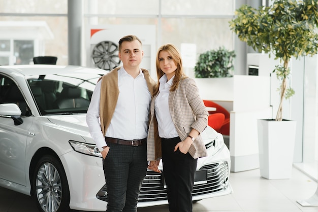 Heureux jeune couple choisit et achète une nouvelle voiture pour la famille chez le concessionnaire.