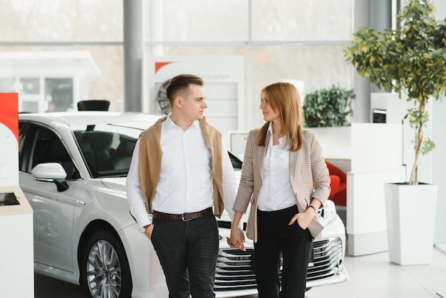 Heureux jeune couple choisit et achète une nouvelle voiture pour la famille chez le concessionnaire.