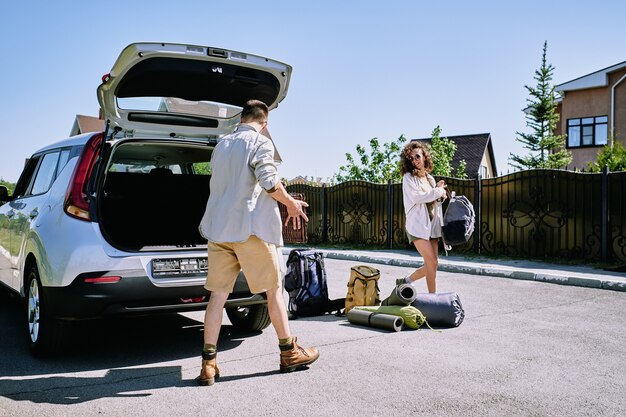 Photo heureux jeune couple la collecte de sacs avec des bagages dans le coffre de la voiture par beau matin d'été tout en voyageant seuls le week-end