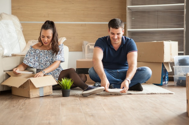 Heureux jeune couple déballant des boîtes dans leur nouvel appartement. Couple assis sur le sol.