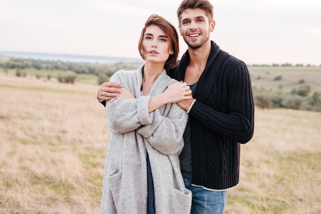 Heureux jeune couple debout et s'embrassant sur le terrain d'herbe en automne