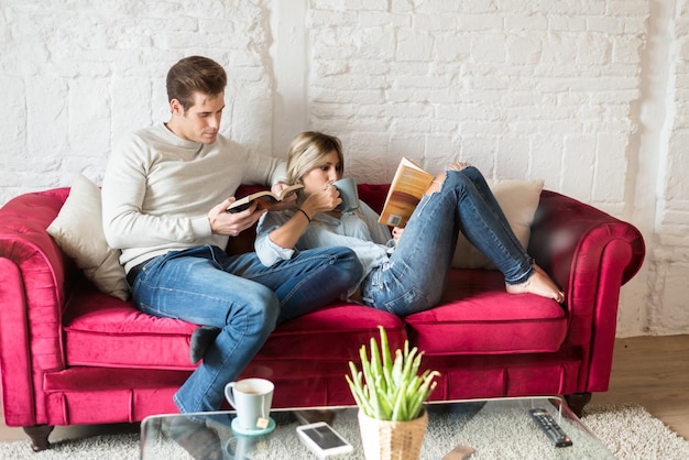 Heureux jeune couple détendu à la maison, assis sur le canapé en lisant un livre