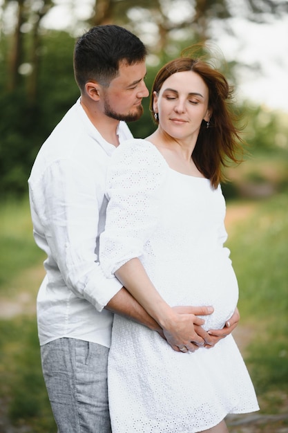 Heureux et jeune couple enceinte embrassant la nature