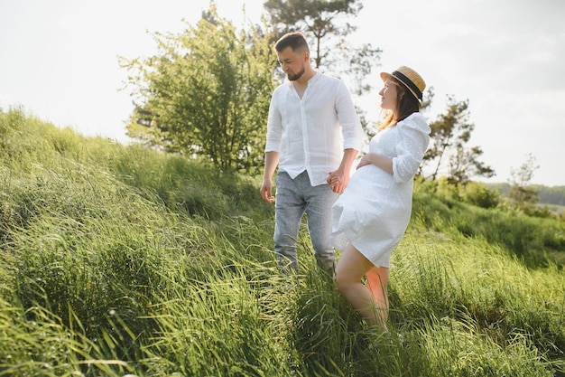 Heureux et jeune couple enceinte embrassant la nature