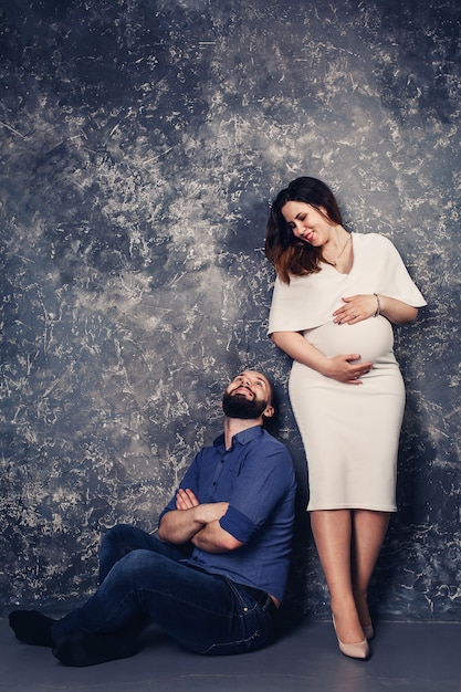 L'heureux jeune couple enceinte en studio sur fond sombre. concept de relation familiale.