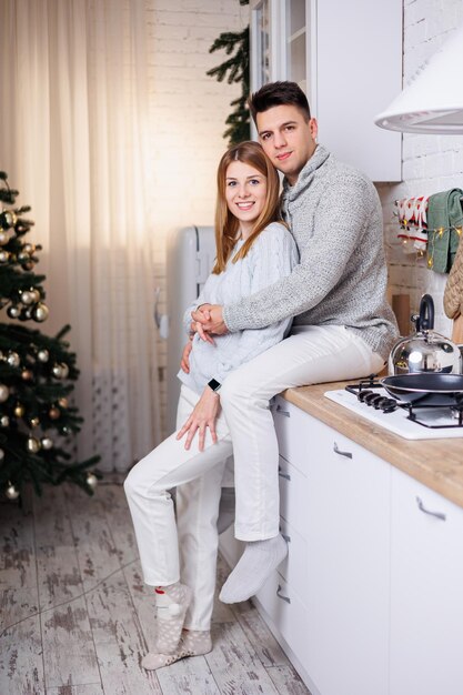 Photo heureux jeune couple étreignant dans la cuisine décorée pour le nouvel an intérieur du nouvel an dans la cuisine cuisine de noël