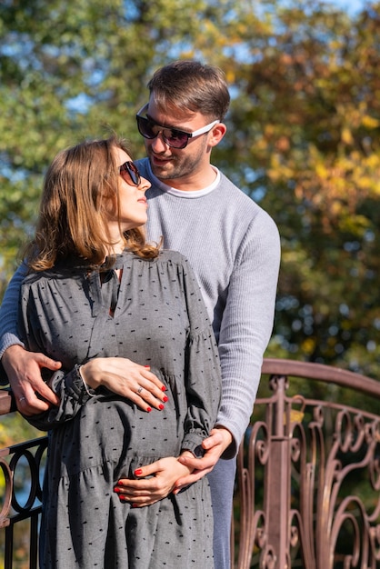 Heureux jeune couple avec une femme enceinte debout ensemble dans une étreinte étroite alors qu'elle berce son bébé bosse dans ses mains