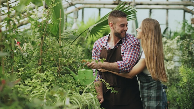 Heureux jeune couple fleuriste en tablier travaillant en serre