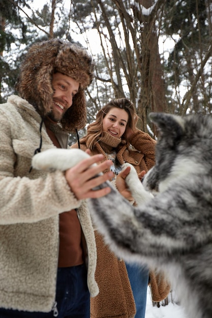 Heureux jeune couple en hiver jouant avec un husky sibérien de race pure et s'amuser dans la forêt de pins enneigée