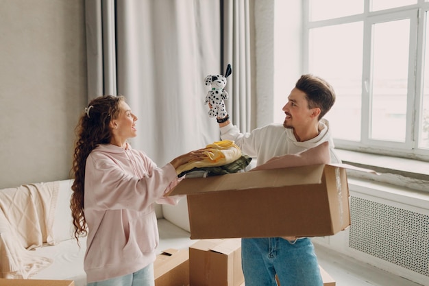 Heureux jeune couple homme et femme déballant la boîte après avoir déplacé des boîtes en carton vers un nouvel appartement