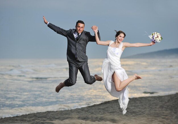 heureux jeune couple juste marié célébrant et s'amusant au magnifique coucher de soleil sur la plage