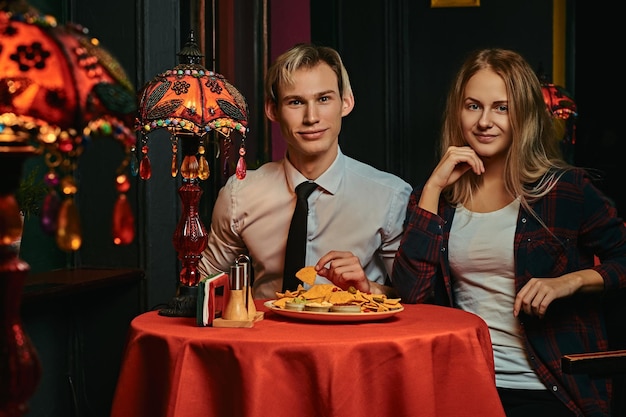 Heureux jeune couple mangeant des nachos lors de rencontres au restaurant mexicain.