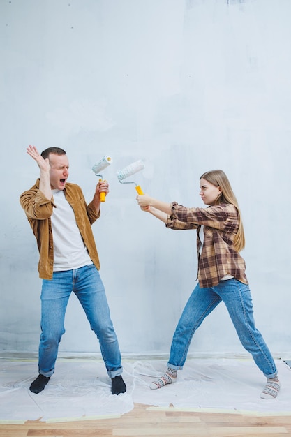 Heureux jeune couple marié amoureux en chemises faisant des rénovations rénovant des murs en peignant avec un rouleau à peinture blanc se préparant à emménager dans une nouvelle maison mise au point sélective