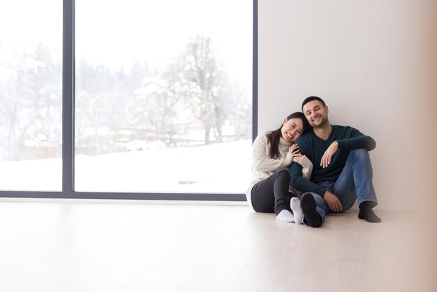 heureux jeune couple multiethnique assis près de la fenêtre à la maison par une froide journée d'hiver