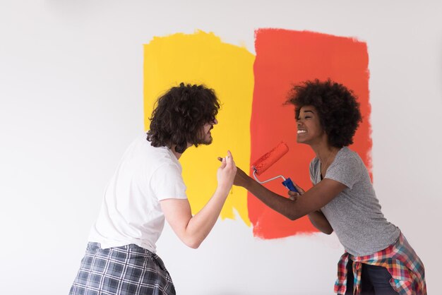 heureux jeune couple multiethnique peignant le mur intérieur de la nouvelle maison