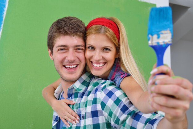 Photo heureux jeune couple peint en vert et bleu le mur blanc de leur nouvelle maison