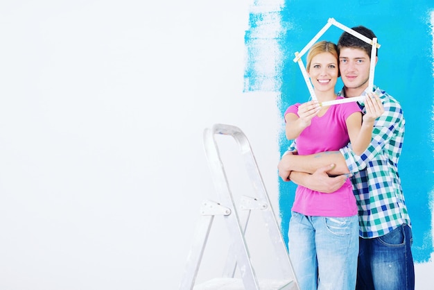 Photo heureux jeune couple peint en vert et bleu le mur blanc de leur nouvelle maison