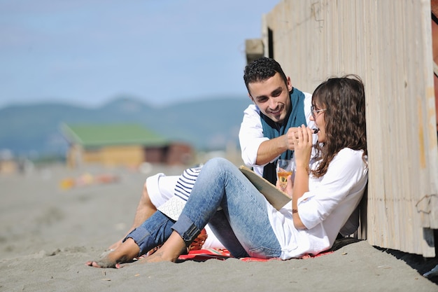 heureux jeune couple profitant d'un pique-nique sur la plage et passer du bon temps pendant les vacances d'été