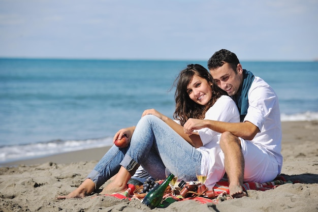 heureux jeune couple profitant d'un pique-nique sur la plage et passer du bon temps pendant les vacances d'été