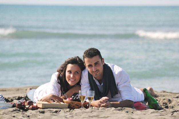 heureux jeune couple profitant d'un pique-nique sur la plage et passer du bon temps pendant les vacances d'été