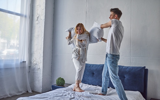 Heureux jeune couple s'amuse dans la chambre. Profiter de la compagnie les uns des autres. Sauter sur le lit pendant une bataille d'oreillers