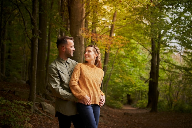 Photo heureux jeune couple se regardant embrassant sur un beau chemin dans une forêt