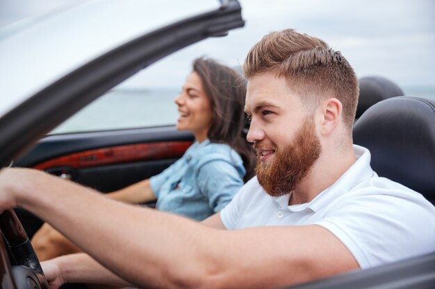 Heureux jeune couple souriant assis à l'intérieur de leur décapotable