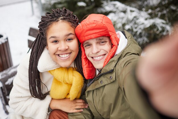 Heureux jeune couple souriant à la caméra du téléphone mobile en journée d'hiver à l'extérieur