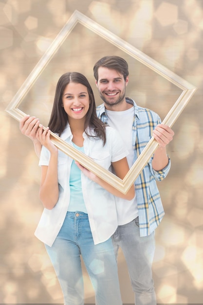 Heureux jeune couple tenant un cadre photo contre le modèle de conception de points lumineux lumineux