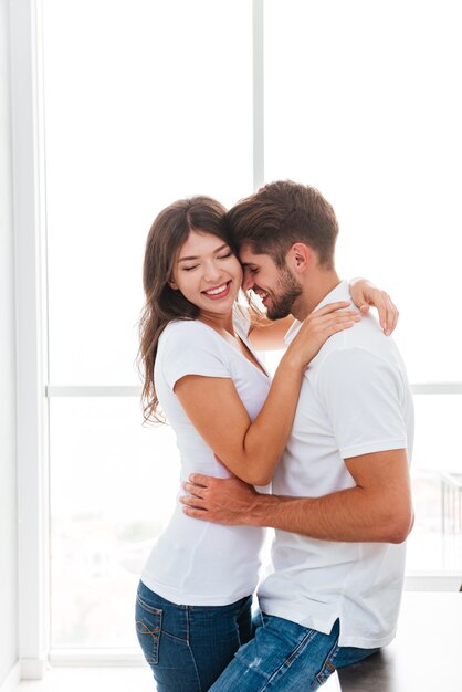 Heureux jeune couple tendre souriant et s'embrassant à la maison