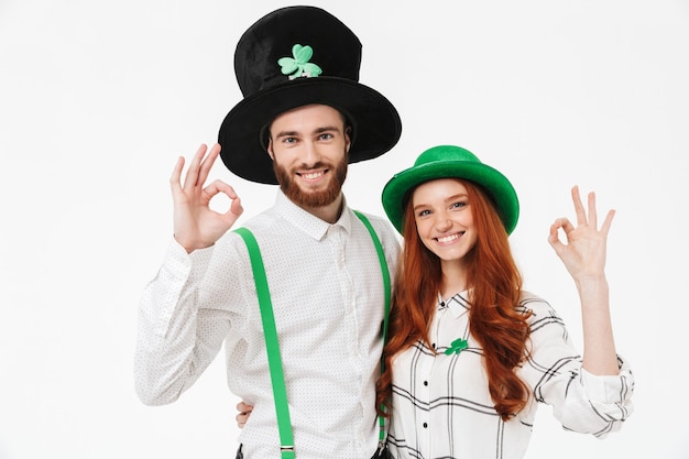 Heureux jeune couple vêtu de costumes, célébrant la Saint-Patrick isolé sur mur blanc, s'amusant ensemble