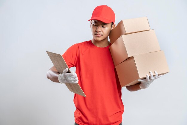 Heureux jeune courrier tenant une boîte en carton et regardant la liste en se tenant debout sur fond blanc