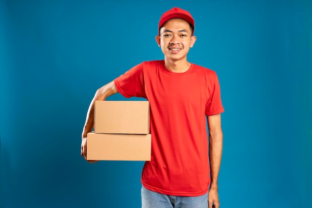 Heureux jeune courrier tenant une boîte en carton et souriant debout sur fond bleu