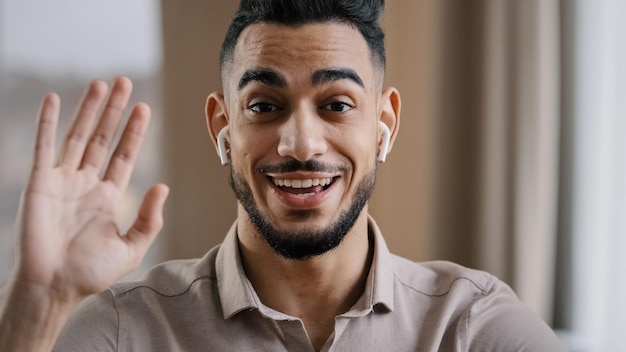 Heureux jeune entraîneur arabe blogueur porte des écouteurs sans fil dire bonjour à l'enregistrement des abonnés à la caméra