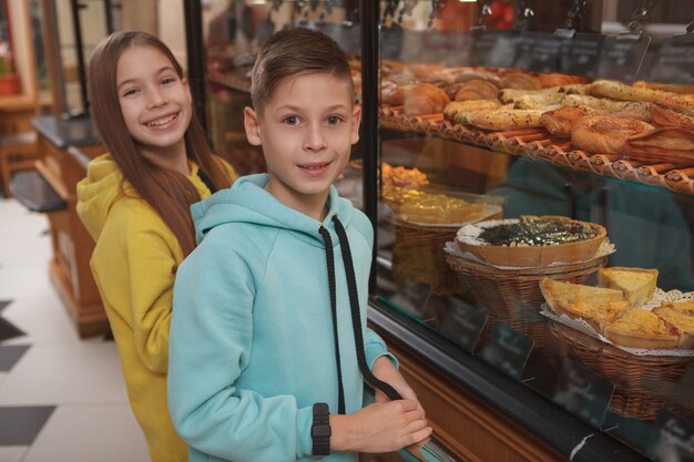 Heureux jeune frère et sœur jumeau souriant et achetant de délicieuses pâtisseries à la boulangerie locale,