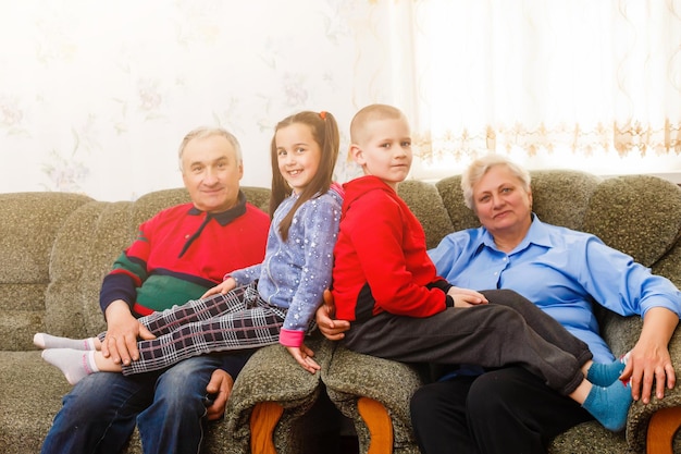 Heureux jeune garçon et fille avec leurs grands-parents rieurs souriant à la caméra alors qu'ils posent ensemble à l'intérieur