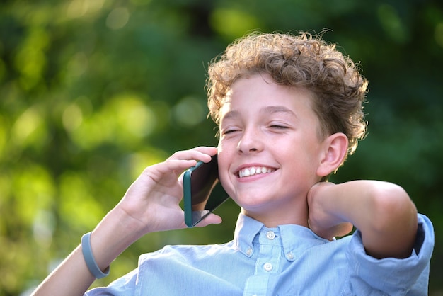 Heureux jeune garçon parlant sur téléphone portable à l'extérieur dans le parc d'été