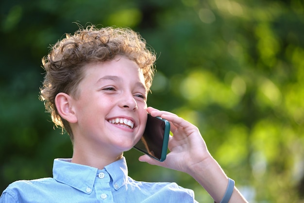 Heureux jeune garçon parlant sur téléphone portable à l'extérieur dans le parc d'été