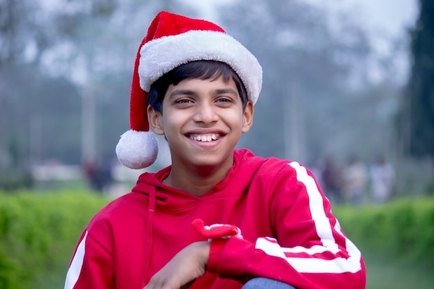 Heureux jeune garçon séduisant en casquette de père Noël - concept de Noël. En regardant la caméra joyeusement